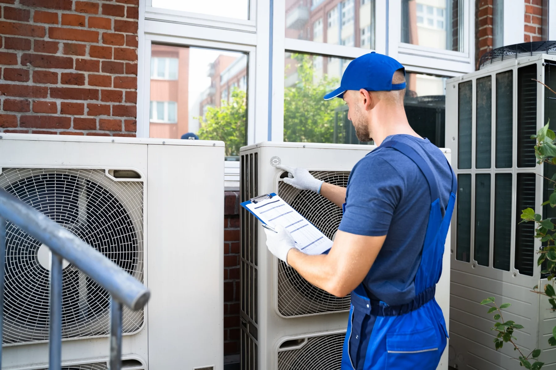HVAC technician inspecting outdoor air-conditioning equipment with a checklist
